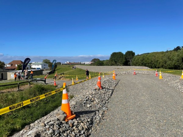 A path along the top of a stopbank with road cones and caution tape.